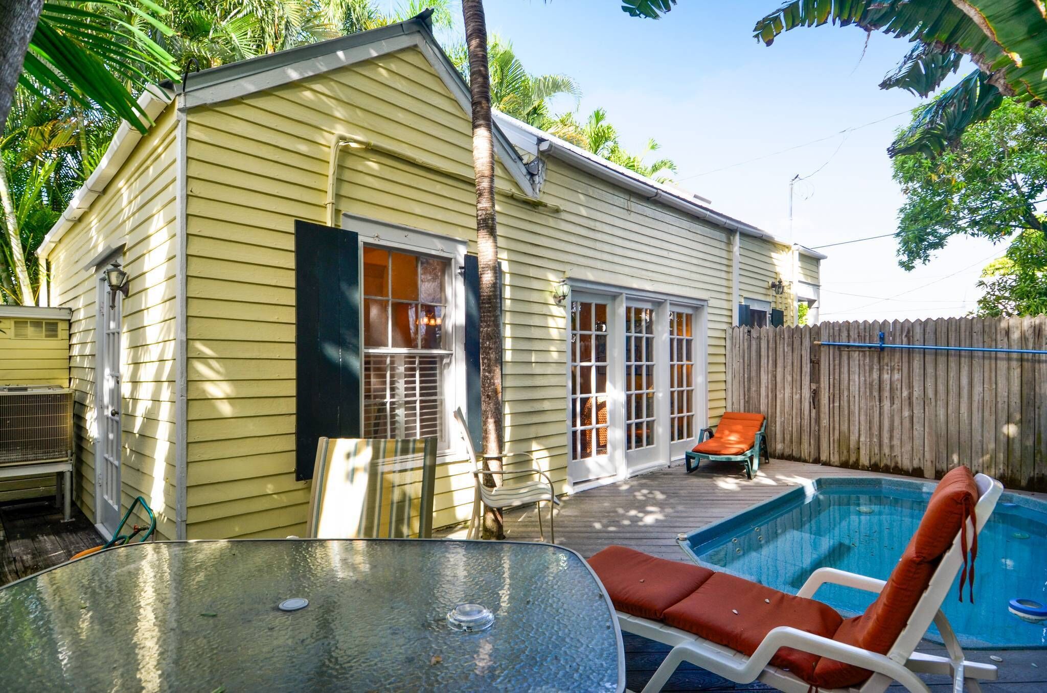 A yellow house with a pool, a covered patio, and a wooden fence.