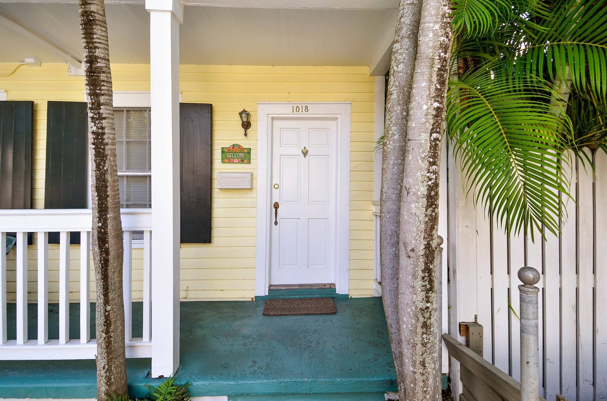 A yellow house with a white door marked "1018" and a welcome sign.