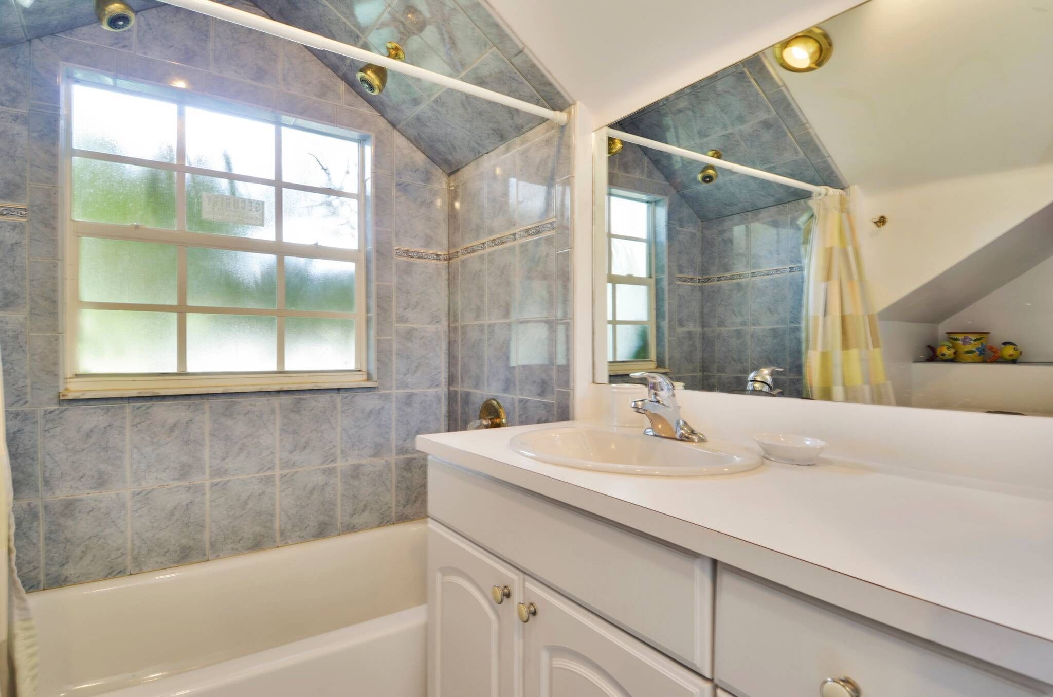 A bathroom with a large window, a bathtub, and a vanity with a sink.