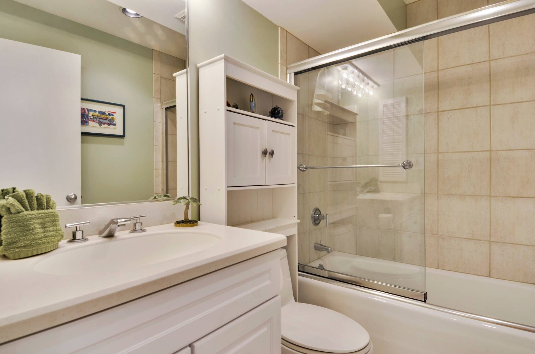A bathroom with a glass-enclosed shower, a white sink with two faucets, and a toilet.