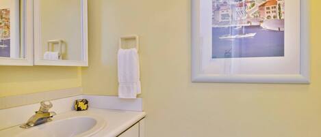 Un baño con lavamanos, espejo y un cuadro enmarcado que muestra una escena costera.