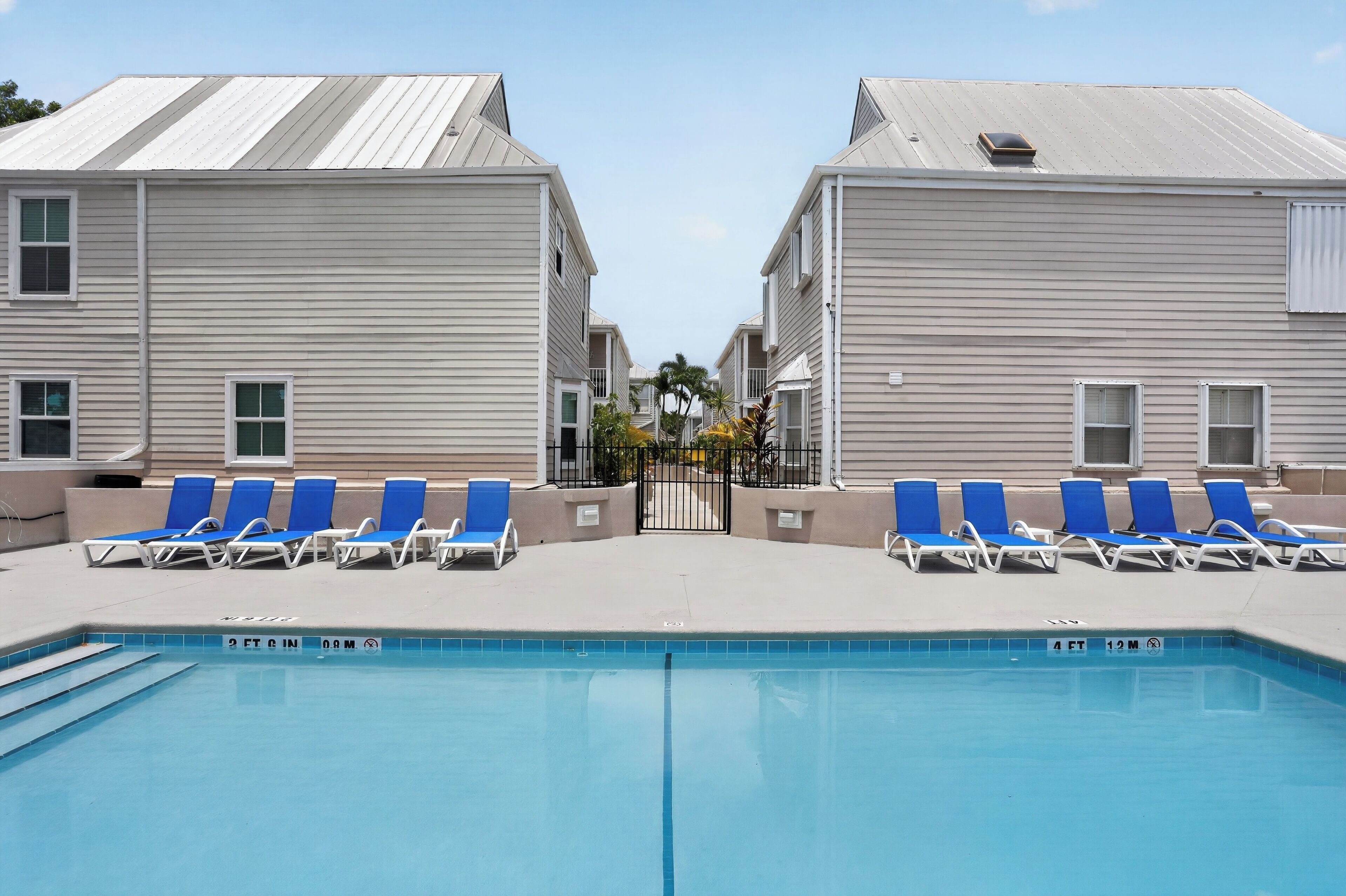 A swimming pool with lounge chairs, a gated entrance, and two-story buildings with a flat roof.