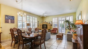 A spacious living room with a fireplace, dining area with wooden chairs, and large windows with blinds. - Truman's Hideaway | Top Location w/ Patio, Pool Access & BBQ | Month Long Stays (Key West)