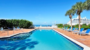 A swimming pool with lounge chairs and palm trees, a cruise ship in the background, and a clear blue sky. - Truman's Hideaway | Top Location w/ Patio, Pool Access & BBQ | Month Long Stays (Key West)