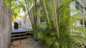 Une terrasse en bois avec des marches menant à un espace abrité, le tout entouré d’une végétation tropicale luxuriante.
