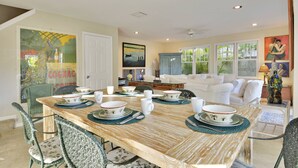 A dining area with a wooden table set for six, surrounded by wicker chairs. - Artist Garden | Great Location w/ Balcony, Shared Pool & BBQ! | Month Long Stays (Key West)