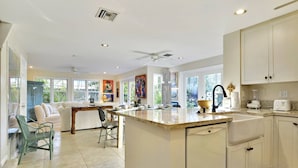 A spacious kitchen with a central island, white cabinetry, and large windows offering views of greenery. - Artist Garden | Great Location w/ Balcony, Shared Pool & BBQ! | Month Long Stays (Key West)