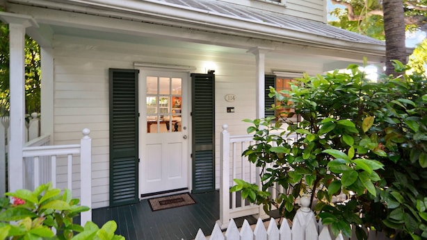 A white house with green shutters, a porch, and a white picket fence. - Artist Garden | Great Location w/ Balcony, Shared Pool & BBQ! | Month Long Stays (Key West)