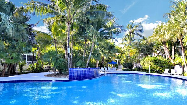 Een helderblauw zwembad omringd door palmbomen en ligstoelen.