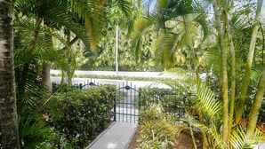 A pathway leading through a lush garden with various tropical plants and a metal gate. - Pool + Walk to Duval & Fort Zachary | Monthly Stays | Key West Found (Key West)