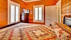Ein Schlafzimmer mit Holzvertäfelung, einem Bett mit Blumenquilt, einem Schminktisch, einem Fernseher und einer Tür.