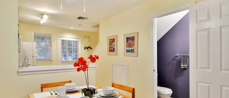 A dining area with a table set for four, a ceiling fan, and a view of the bathroom.
