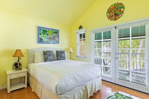 A bedroom with a large bed, a nightstand, a lamp, a window with blinds, and a painting on the wall. - Southard Getaway | Covered Patio, Great Location, Shared Pool | Month Long Stays (Key West)