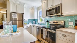 Une cuisine moderne avec des armoires blanches, des appareils en acier inoxydable et un pare-feu turquoise.