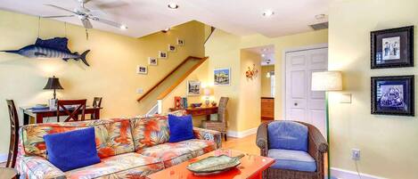 A living room with a sofa, a chair, a table, a ceiling fan, and a staircase.