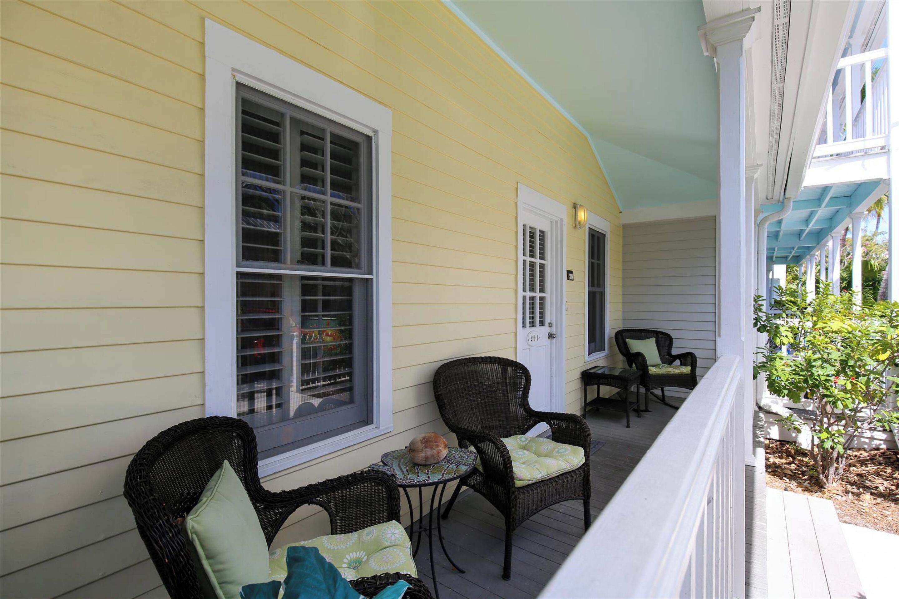 A porch with wicker chairs and a small table, a window with shutters, and a door.
