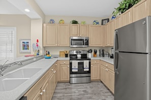 A modern kitchen with wooden cabinets, stainless steel appliances, and a granite countertop. - Place to Relax by AvantStay | Shared Pool | 3 Miles to Smather's Beach (Key West)