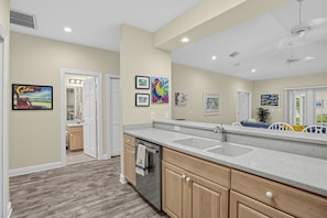A modern kitchen with a large island, wooden cabinets, and a view into the adjacent bathroom. - Place to Relax by AvantStay | Shared Pool | 3 Miles to Smather's Beach (Key West)