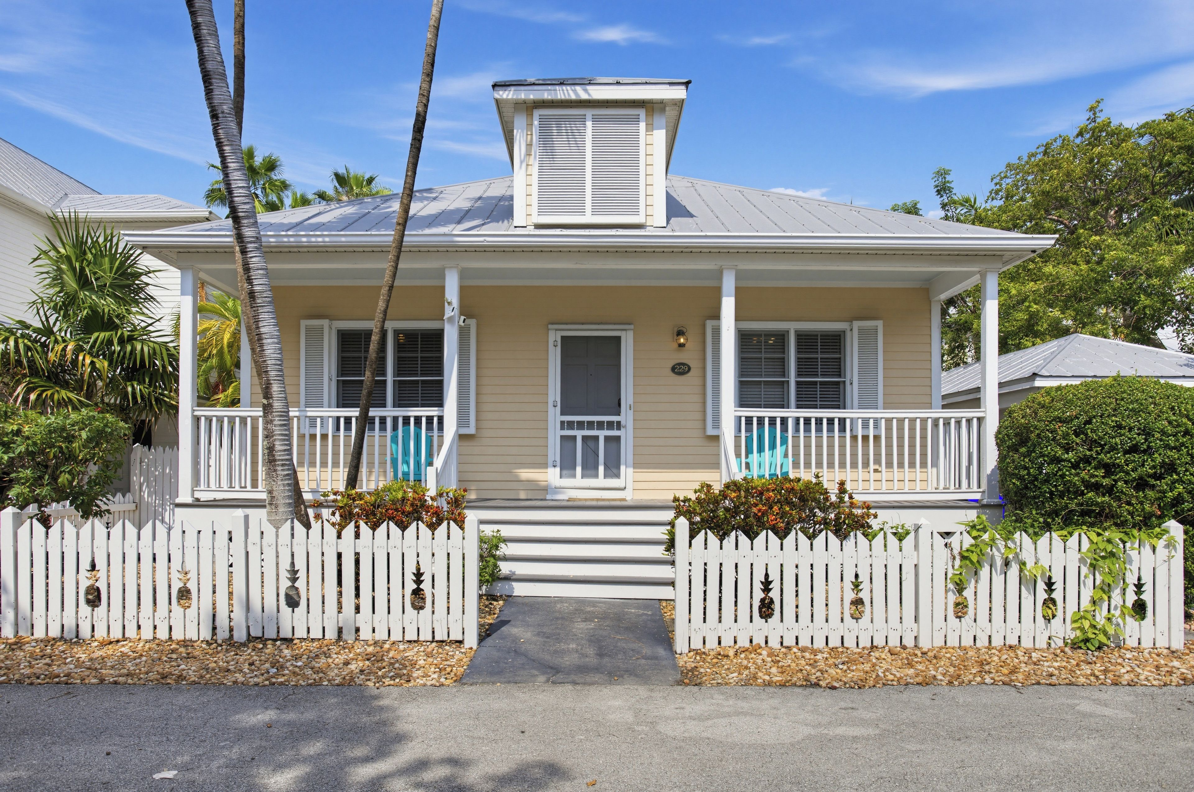 A charming cottage exterior welcomes you with a covered front porch, tropical landscaping, and classic coastal character.