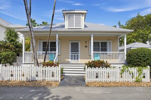 A two-story house with a front porch, a small garage, and a white picket fence. - Place to Relax by AvantStay | Shared Pool | 3 Miles to Smather's Beach (Key West)