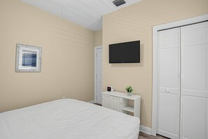 A bedroom with a bed, a television mounted on the wall, a small white cabinet, and a wardrobe.