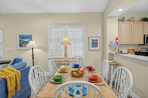 A dining area with a wooden table set for four, surrounded by white chairs.