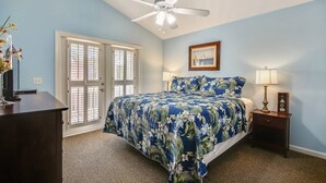 A bedroom with a bed, a ceiling fan, a nightstand, a lamp, and a door with glass panels.