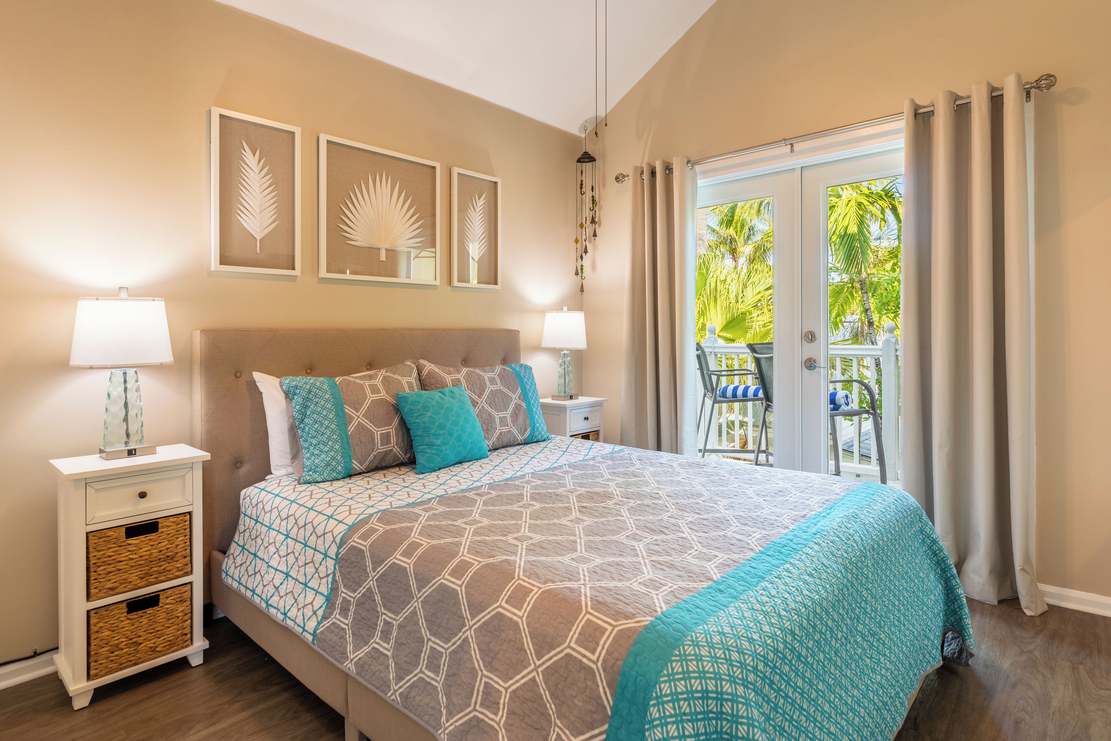 A bedroom with a large bed, two bedside tables, a nightstand, and a view of the outdoors through a sliding door.