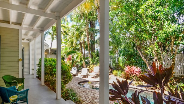 Un patio techado con mobiliario exterior y zona de piscina rodeada de exuberante vegetación.