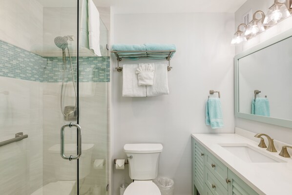 A bathroom with a glass shower enclosure, a toilet, a sink with a vanity, and a mirror.