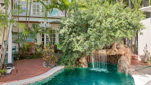 Una piscina con cascada rodeada de exuberante vegetación y un edificio blanco con balcones.
