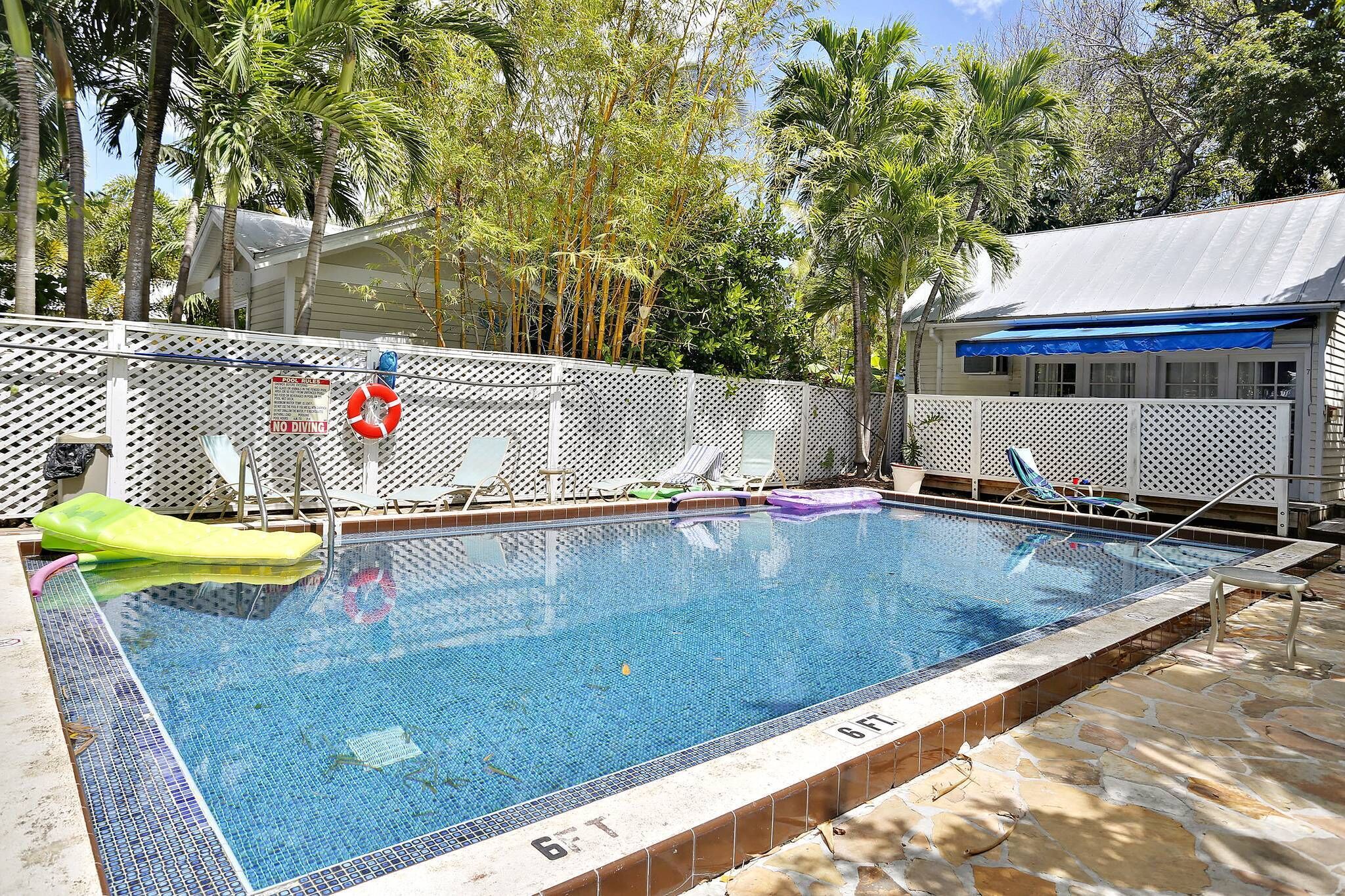 A swimming pool with a white fence, lounge chairs, and a lifebuoy.