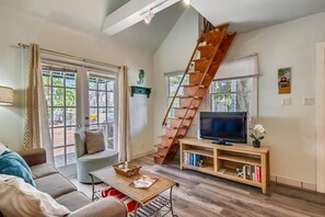 A spacious living room with a wooden staircase, a comfortable sofa, a television on a wooden stand, and a bookshelf. - Ibis by AvantStay | Close to Duval Street w/ Shared Pool | Month Long Stays Only (Key West)