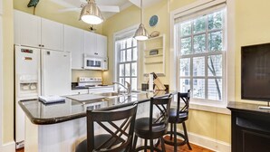 A kitchen with white cabinets, a microwave, a refrigerator, a sink, and a bar area with stools. - Lazy Gecko by AvantStay | Walk to Duval St in Key West! | Month Long Stays Only (Key West)