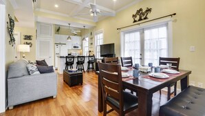 A spacious living room with a grey sofa, wooden dining table set for four, and a kitchen in the background. - Lazy Gecko by AvantStay | Walk to Duval St in Key West! | Month Long Stays Only (Key West)