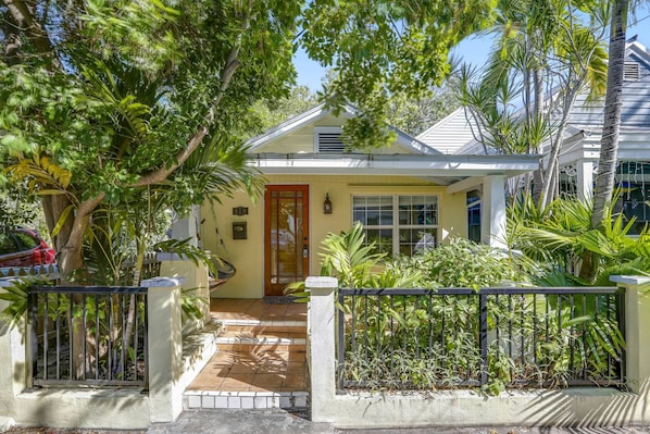 A two-story house with a front porch, a small garden, and a metal gate.