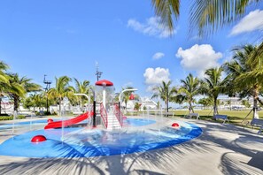 A water park with slides and water features, surrounded by palm trees and a clear sky.