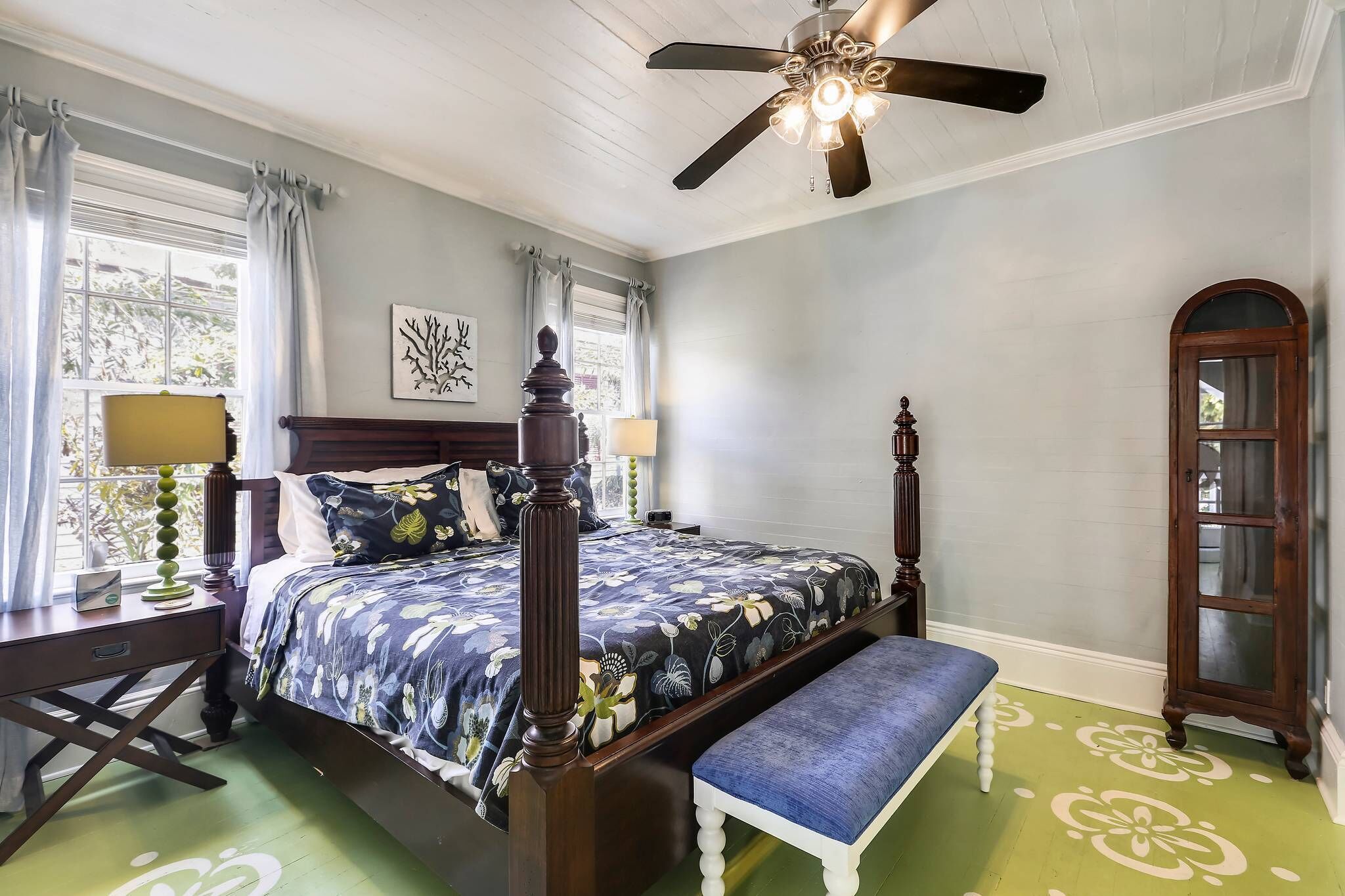 A bedroom with a four-poster bed, a bench, a nightstand, a lamp, and a window with curtains.