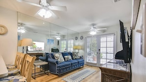 A living room with a blue sofa, wooden chairs, a glass coffee table, and a television. - Always Your Paradise | Shared Pool | Near Zachary Beach | Month-Long Stays (Key West)