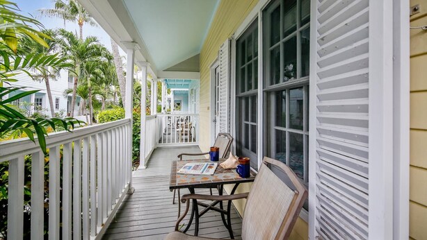 A covered porch with a table and chairs, a view of a building, and a railing. - Always Your Paradise | Shared Pool | Near Zachary Beach | Month-Long Stays (Key West)