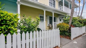 A two-story house with a porch, a white picket fence, and various plants. - Always Your Paradise | Shared Pool | Near Zachary Beach | Month-Long Stays (Key West)
