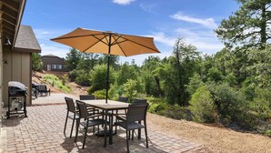 Une terrasse extérieure avec une table et des chaises en briques, un grand parasol et un barbecue.