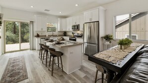 Une cuisine moderne avec des meubles blancs, des appareils en acier inoxydable et un îlot central doté de tabourets de bar.