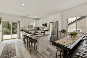 Una cocina moderna con armarios blancos, electrodomésticos de acero inoxidable y una isla central con taburetes de bar.