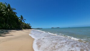 A beach with clear blue water, sandy shore, and palm trees.
