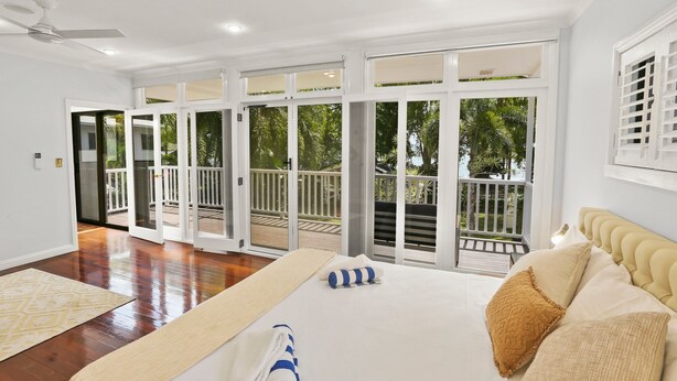 A spacious bedroom with a large bed, a balcony with a view of greenery, and a sliding glass door leading to an outdoor area.