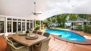 A covered outdoor area with a pool, wicker furniture, and a gazebo.