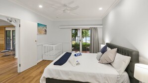 A bedroom with a bed, a crib, a ceiling fan, a window with curtains, and a view of the outdoors.