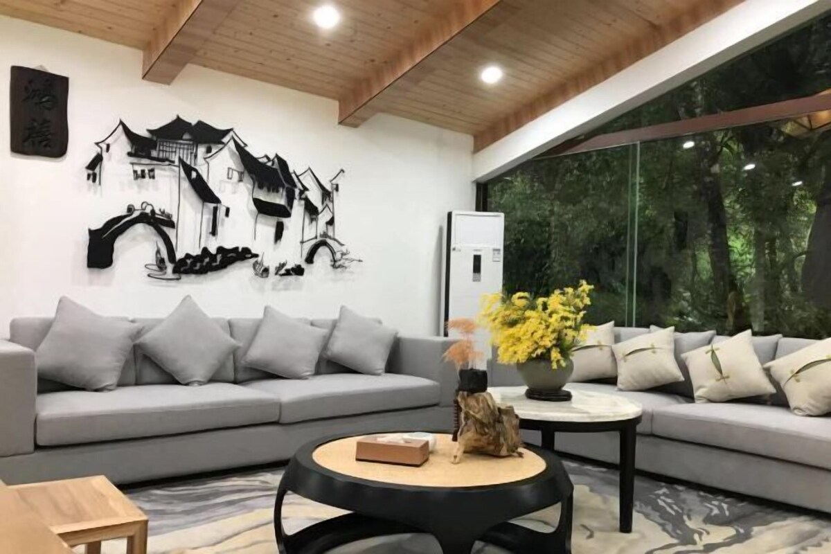 Una sala de estar moderna con un sofá gris, una mesa redonda de centro y una obra de arte colgante que representa un edificio tradicional.