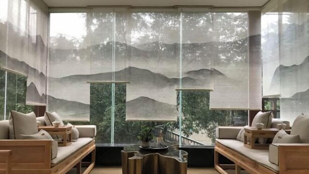 Un salon moderne comprenant un ensemble de canapés, une table basse et une vue sur un paysage montagneux, visible à travers des rideaux légers.